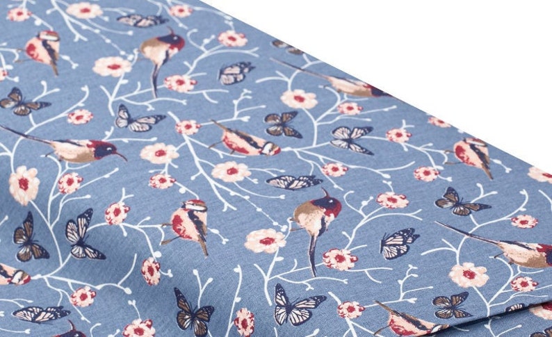May include: Blue fabric with a repeating pattern of white branches, pink flowers, butterflies, and small birds. The birds are a light brown with red accents.