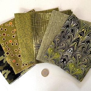 Può includere: Una collezione di sei campioni di tessuto piegati in varie tonalità di verde oliva e lime. I motivi includono mimetico con teschio, cerchi arancioni, texture crepata, linee a griglia, spina di pesce e un design marmorizzato, con una moneta per scala.