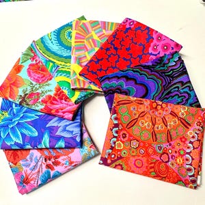 Peut inclure: Une collection de carrés de tissu pliés disposés en éventail. Les textiles présentent des motifs vibrants et multicolores, notamment des motifs floraux, des formes abstraites tourbillonnantes et des designs géométriques en rouge, orange, bleu, violet et vert.
