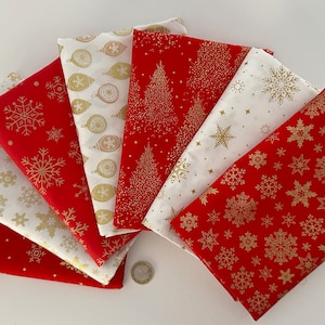 Könnte beinhalten: Eine Sammlung von sieben gefalteten Stoffquadraten, die fächerförmig angeordnet sind. Die Stoffe haben rote und weiße Hintergründe mit metallisch goldenen Mustern wie Schneeflocken, Weihnachtsbäumen und Ornamenten. Eine kleine Münze dient als Maßstab.