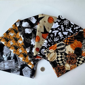 Op de afbeelding: Vijf gevouwen stoffen vierkanten met Halloween-patronen, waaronder grafstenen met tekst, geesten, pompoenen, schedels en spinnenwebben in zwart, oranje, wit en beige. Een kleine ronde metalen munt ligt in het midden voor de schaal.
