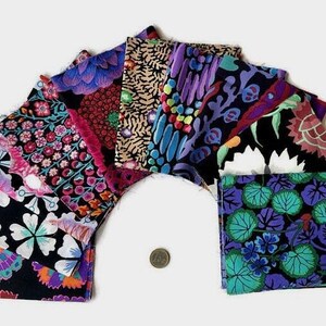 Könnte beinhalten: Eine Sammlung quadratischer Stoffmuster, die fächerförmig angeordnet sind und verschiedene florale und abstrakte Muster in leuchtenden Farben wie Lila, Blau, Pink und Grün auf schwarzem Grund zeigen, mit einer kleinen Silbermünze als Maßstab.