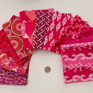 Peut inclure: Un ensemble de carrés de tissu roses aux motifs variés, disposés en éventail. Les motifs comprennent des fleurs, des formes géométriques et des dessins abstraits. Une pièce de monnaie est au centre. Ces tissus sont parfaits pour le patchwork ou la couture.