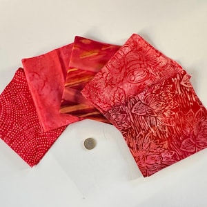 Peut inclure: Cinq carrés de tissu rouge avec des motifs différents. Les carrés sont disposés en forme d'éventail. Le tissu a un motif de style batik.