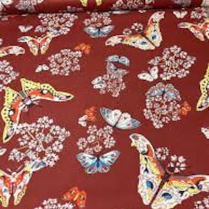 Peut inclure: Tissu rouge avec un motif répété de papillons colorés et de fleurs blanches.