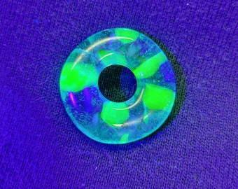 May include: A green and blue glass ring with a hole in the centre. The ring is made of clear glass with green and blue swirls.
