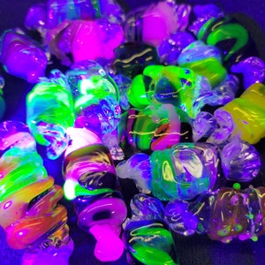 May include: A collection of colourful glass marbles with swirls of green, pink, black, and white. The marbles are illuminated with a blacklight, making them glow brightly.