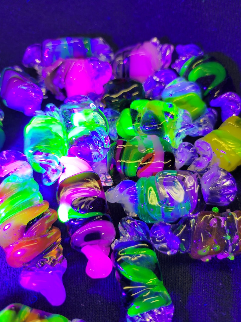 May include: A collection of colourful glass marbles with swirls of green, pink, black, and white. The marbles are illuminated with a blacklight, making them glow brightly.