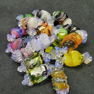 May include: A collection of colourful glass candy-shaped ornaments. The ornaments are made of clear glass with swirls of colour, including blue, green, yellow, orange, and purple.