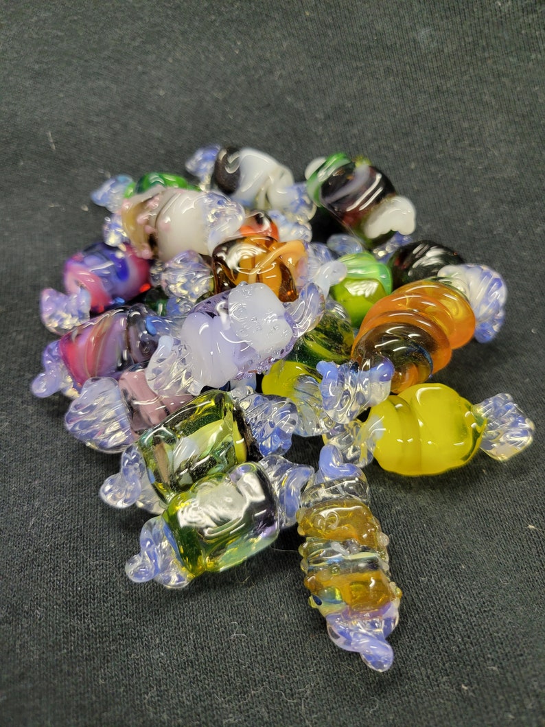 May include: A collection of colourful glass candy-shaped ornaments. The ornaments are made of clear glass with swirls of colour, including blue, green, yellow, orange, and purple.