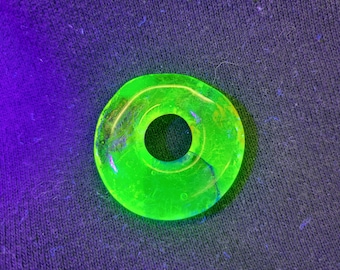 May include: A bright green glass ring with a hole in the centre. The ring is made of uranium glass and glows under a black light.