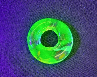 May include: A bright green glass ring with a swirling pattern. The ring has a hole in the centre and is made of clear glass with a green tint.