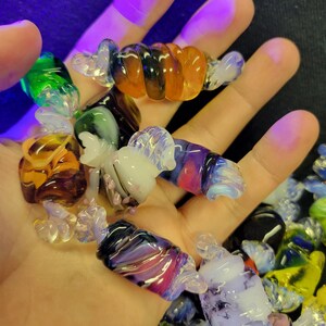 May include: A collection of colourful glass candy cane ornaments. The ornaments are made of clear, green, purple, orange, and white glass. They are twisted and swirled to resemble candy canes.
