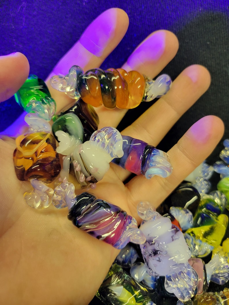 May include: A collection of colourful glass candy cane ornaments. The ornaments are made of clear, green, purple, orange, and white glass. They are twisted and swirled to resemble candy canes.
