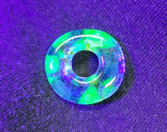 May include: A green and blue iridescent glass donut bead with a hole in the centre.