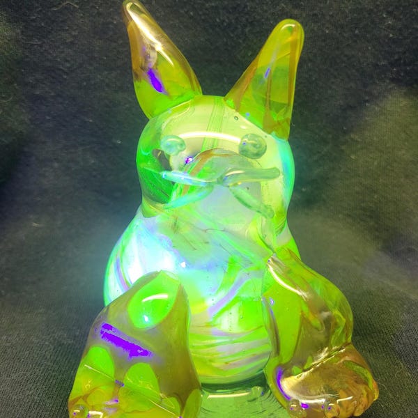 May include: A green glass figurine of a sitting rabbit with iridescent swirls. The rabbit has large ears and a rounded body.