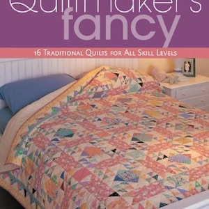 May include: A book titled "Quiltmaker's Fancy" with a purple cover and the text "16 Traditional Quilts for All Skill Levels". The book cover features a photograph of a bed with a colorful patchwork quilt.