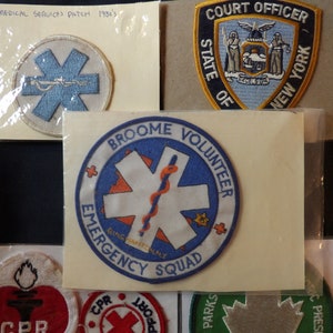 May include: A collection of embroidered patches featuring various designs, including a medical services patch, a court officer patch, and a volunteer emergency squad patch. The patches are displayed on a white background.