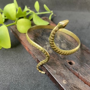 May include: A gold-toned snake-shaped bracelet with a textured surface. The bracelet is open and has a simple design.