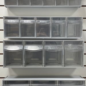May include: A set of clear plastic storage bins with metal frames. The bins are stacked on a white wall with horizontal grooves. The bins are labelled "Steel Plastic".