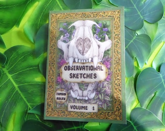 May include: A green book with a gold ornate frame and a skull illustration. The title is "Observational Sketches" with the author "Tamsin Adlev" and "Volume 1" printed on the cover.