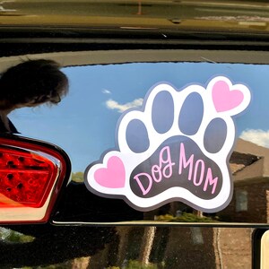 May include: Black and white paw print with the text "Dog Mom" in white script. Two pink hearts are on either side of the paw print.