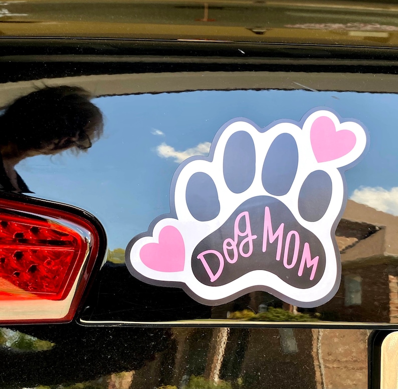 May include: Black and white paw print with the text "Dog Mom" in white script. Two pink hearts are on either side of the paw print.