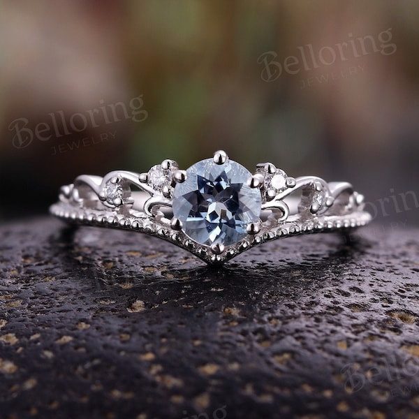 May include: A delicate silver ring featuring a light blue aquamarine centre stone and smaller diamonds set in a crown-like design.