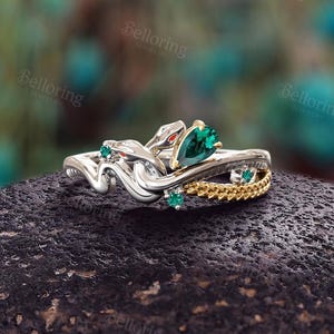 Puede incluir: Un anillo de plata y oro con una piedra preciosa verde y un diseño de serpiente.