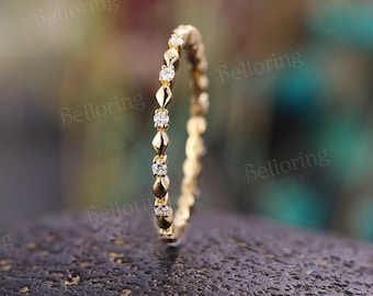 May include: A thin yellow gold band ring featuring a repeating marquise-shaped metal pattern alternating with small, round, clear, sparkling stones set along the outer circumference of the delicate, circular jewelry piece.