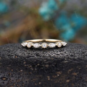 May include: A delicate gold band featuring a row of marquise and round diamonds. The band is set against a dark grey background.