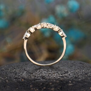 May include: A delicate gold band with five small round diamonds set in a curved row. The band is shown on a dark grey textured surface.