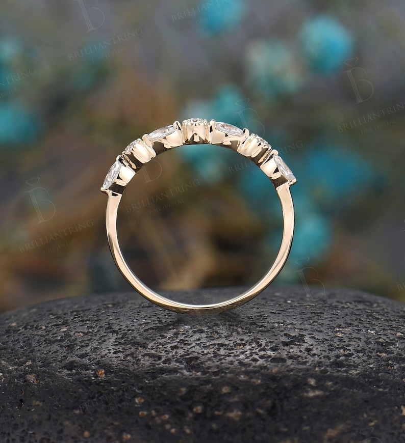 May include: A delicate gold band with five small round diamonds set in a curved row. The band is shown on a dark grey textured surface.