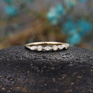 May include: A delicate gold band featuring a row of marquise and round diamonds. The band is set against a dark grey stone.