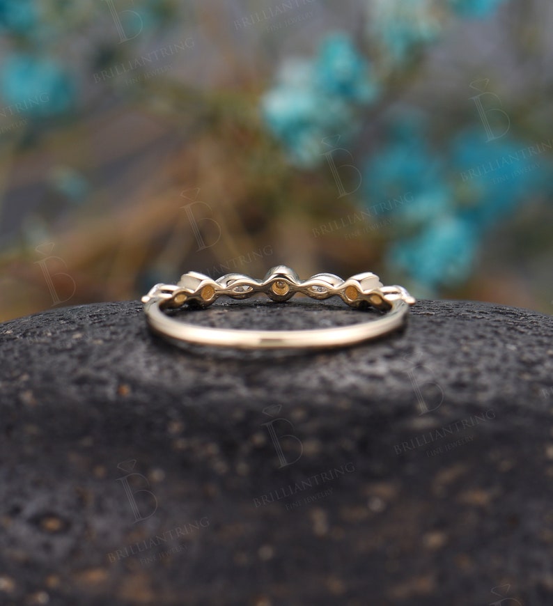 May include: A delicate gold band featuring a row of small, round and oval-shaped gemstones. The band is thin and has a smooth finish.