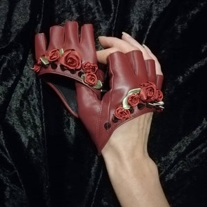 May include: A pair of red leather fingerless gloves with gold accents and red fabric roses.