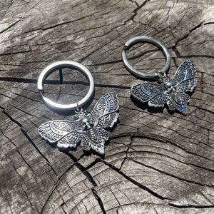 May include: Two silver keychains with detailed, ornate butterfly charms. Each butterfly has a skull design in the center.