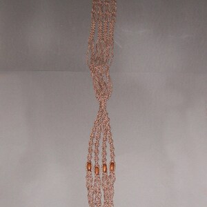 Op de afbeelding: Een lange, bruine macramé plantenhanger met houten kralen. De hanger is gemaakt van meerdere strengen touw die aan elkaar geknoopt zijn om een decoratief patroon te creëren.