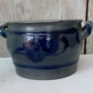 Könnte beinhalten: Ein dunkelblauer Keramiktopf mit zwei gebogenen Griffen. Der Topf hat einen abgerundeten Körper und einen dunklen Rand. Die Außenseite hat eine glänzende Oberfläche mit einer dunkelblauen Glasur und einem dunkleren Boden.