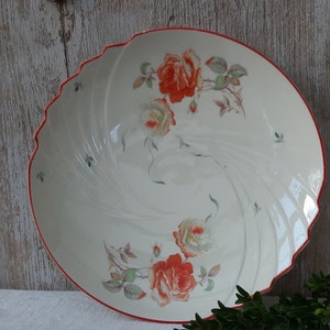 Pode incluir: Uma tigela de servir de cerâmica branca com borda ondulada e borda vermelha. A tigela é decorada com rosas laranja e creme e folhas verdes. A tigela tem aproximadamente 30 cm de diâmetro.