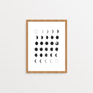 May include: A framed black and white print of the phases of the moon. The print is in a light wood frame and has a white background.