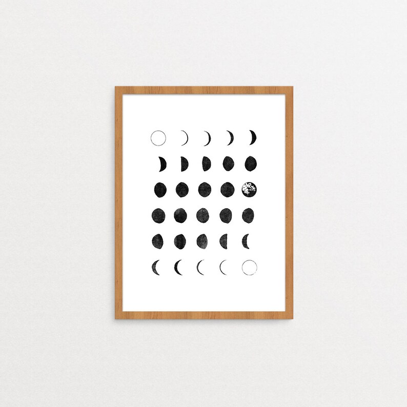 May include: A framed black and white print of the phases of the moon. The print is in a light wood frame and has a white background.