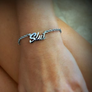 May include: A silver chain bracelet with the word "Slut" spelled out in cursive.