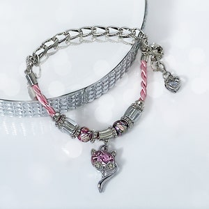 May include: A pink and silver charm bracelet with a cat charm, heart charm, and pink beads.