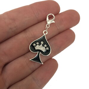 May include: A silver charm with a black spade design and a rhinestone crown. The charm has a lobster claw clasp.