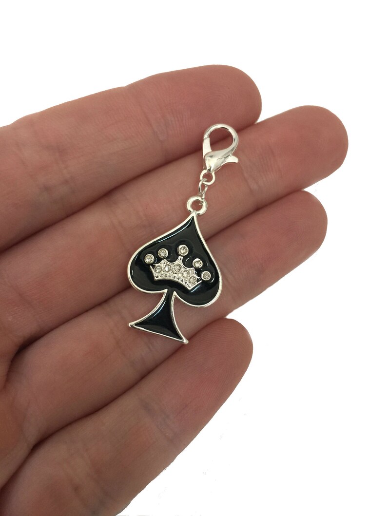 May include: A silver charm with a black spade design and a rhinestone crown. The charm has a lobster claw clasp.