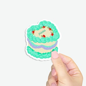 Könnte beinhalten: Ein Aufkleber mit einem grünen und weißen Kuchen, auf dem das Wort "Pisces" steht. Der Kuchen ist mit roten Kirschen verziert.
