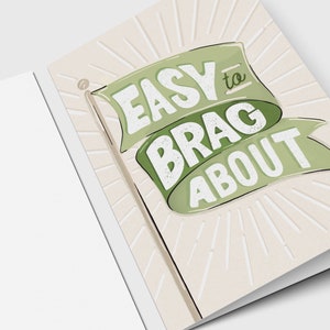 May include: Greeting card with a light beige background and a green banner that reads "EASY to BRAG ABOUT". The banner is designed to look like a flag. The card is open, showing the inside.