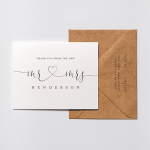May include: A white thank you card with the text "Thank you from the new Mr & Mrs Henderson" in black script font with a heart symbol between the words "Mr" and "Mrs". The card is sitting on top of a brown envelope with the text "anglee & austin 1234 West Main Street Somerville NJ 08876" in black script font.