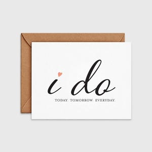 May include: A white greeting card with a brown envelope featuring the black cursive text i do, a small pink heart above the letter i, and the text TODAY. TOMORROW. EVERYDAY. printed in a smaller black sans-serif font underneath the main phrase.